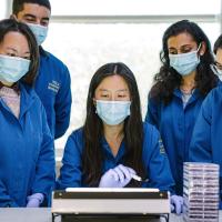 A group of UCLA researchers led by Melody Li gathers around a piece of laboratory equipment 