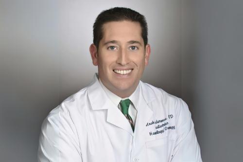 A doctor in a whitecoat smiles for a headshot.
